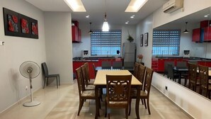 Ein moderner Essbereich mit einem rechteckigen Tisch und Stühlen, einem Standventilator und einem großen Spiegel an der Wand.