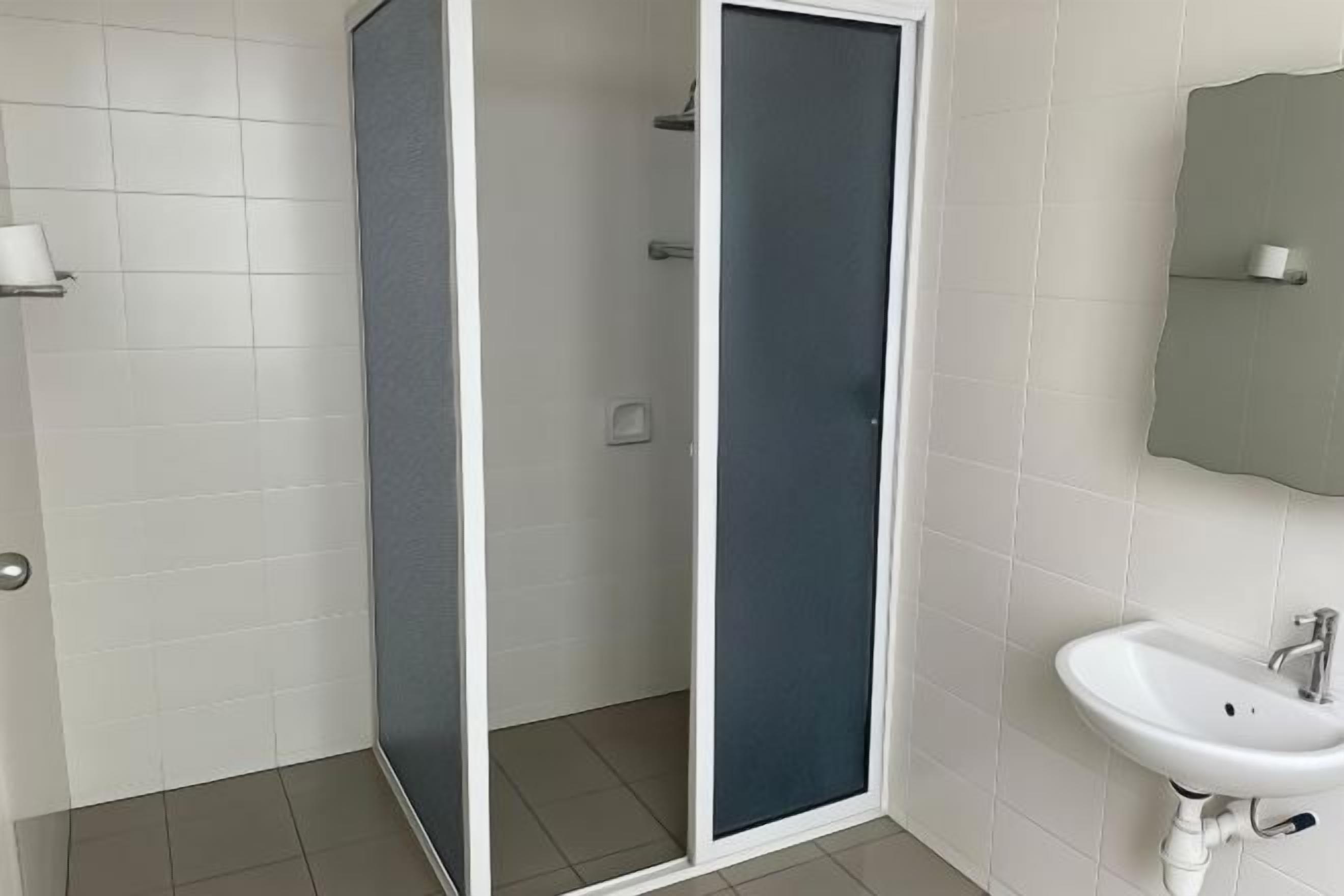 A bathroom with white tiled walls, a white sink, and a shower enclosure with a glass door.