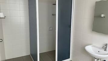 A bathroom with white tiled walls, a white sink, and a shower enclosure with a glass door.