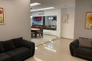 Una sala moderna con dos sofás, un comedor con mesa y sillas, y una cocina al fondo.