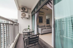 A balcony with a table and chairs, a sofa inside the adjacent room, and two air conditioning units mounted on the wall. - Perling 8scape 3BR Comfy Zone nr Bukitindah/Sutera (Johor Bahru)