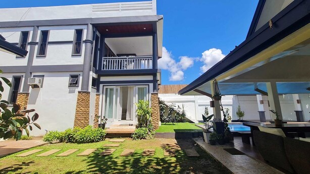 A modern two-story house with a balcony, a front door, and a small garden area with potted plants. - OYO 1175 Casa Ana (Manila)