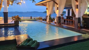 A pool area with a view of the sea, a covered seating area with plants, and a table with towels. - OYO 1175 Casa Ana (Manila)