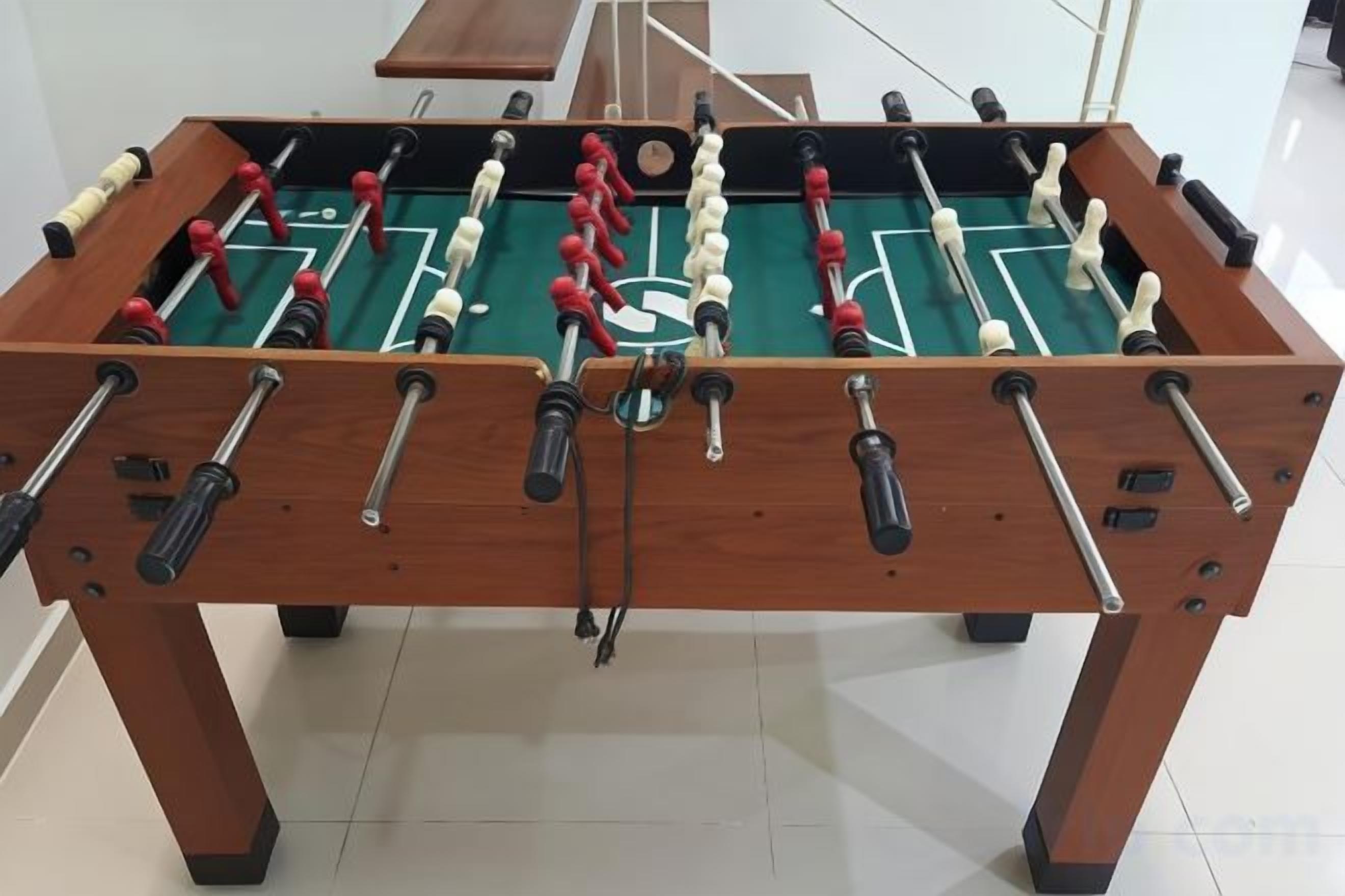 A wooden foosball table with a green playing surface and red and white player figures.