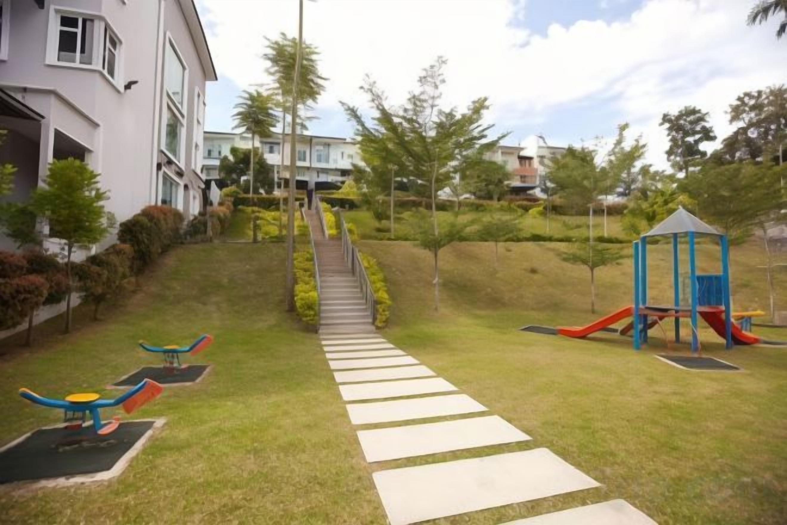 A playground with slides and swings, a pathway leading to a building, and a small hill with trees.