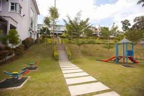 A playground with slides and swings, a pathway leading to a building, and a small hill with trees. - Shamrock Beach Villa Penang No20 Sleeps 22 (Tanjung Bungah)