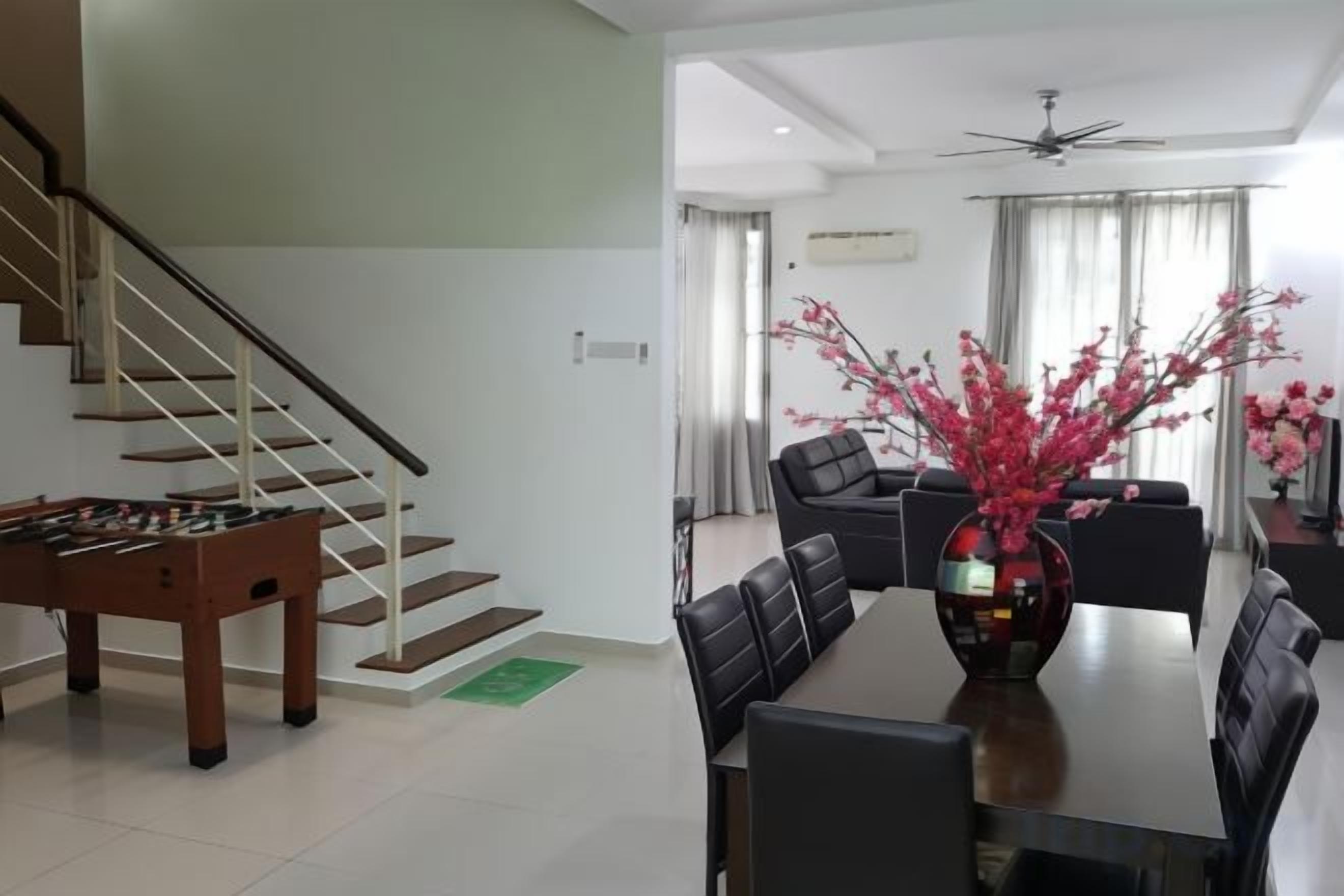 A modern living room with a dining table, chairs, a sofa, a staircase, and a foosball table.