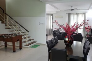 A modern living room with a dining table, chairs, a sofa, a staircase, and a foosball table. - Shamrock Beach Villa Penang No20 Sleeps 22 (Tanjung Bungah)
