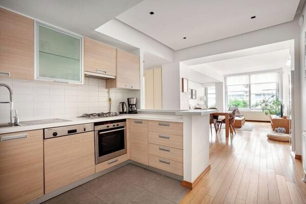 A modern kitchen with light wood cabinets, a built-in oven, and a large window providing natural light. - NOA - Süngü 1 (Istanbul)