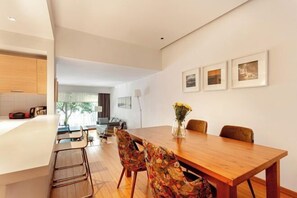 A modern dining area with a wooden table, floral chairs, and a vase with flowers. There are framed pictures on the wall and a view of the living room in the background. - NOA - Süngü 1 (Istanbul)