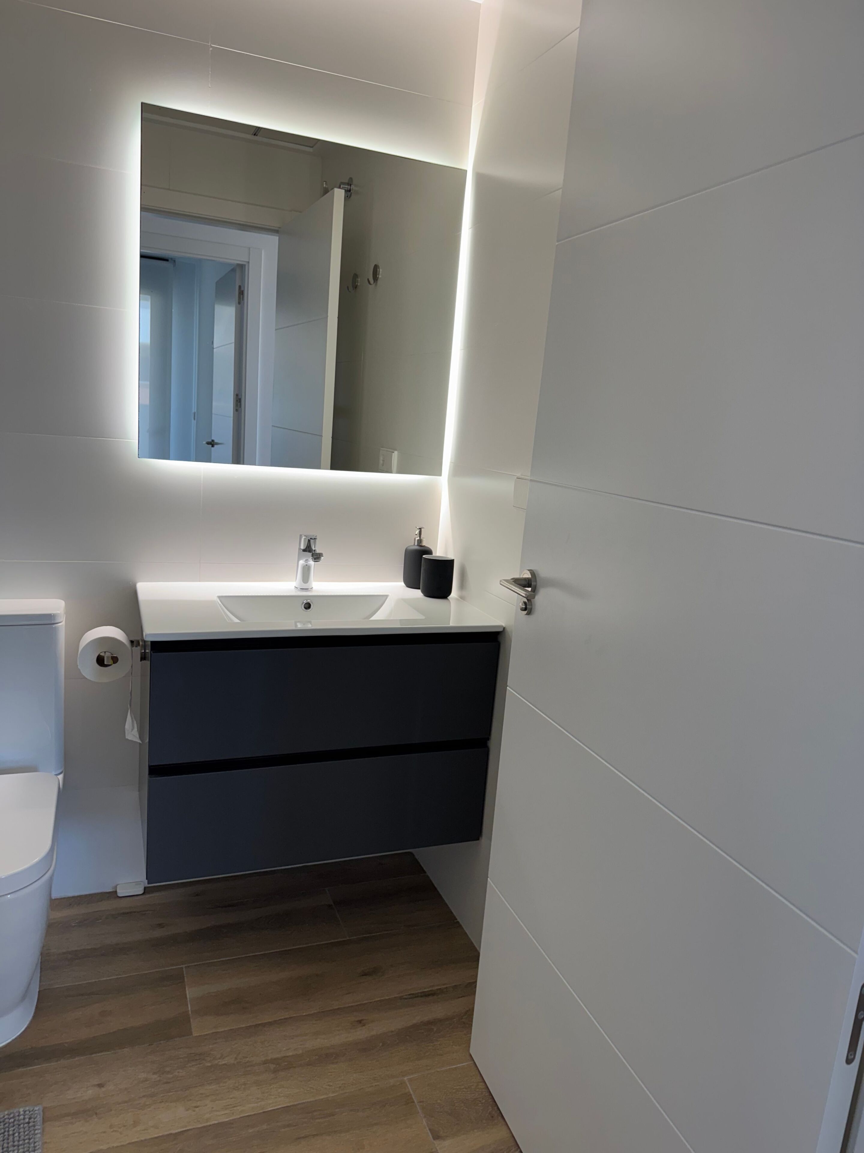 Un baño moderno con un lavamanos blanco, un mueble oscuro y un espejo con iluminación debajo.