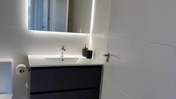 Un baño moderno con un lavamanos blanco, un mueble oscuro y un espejo con iluminación debajo.
