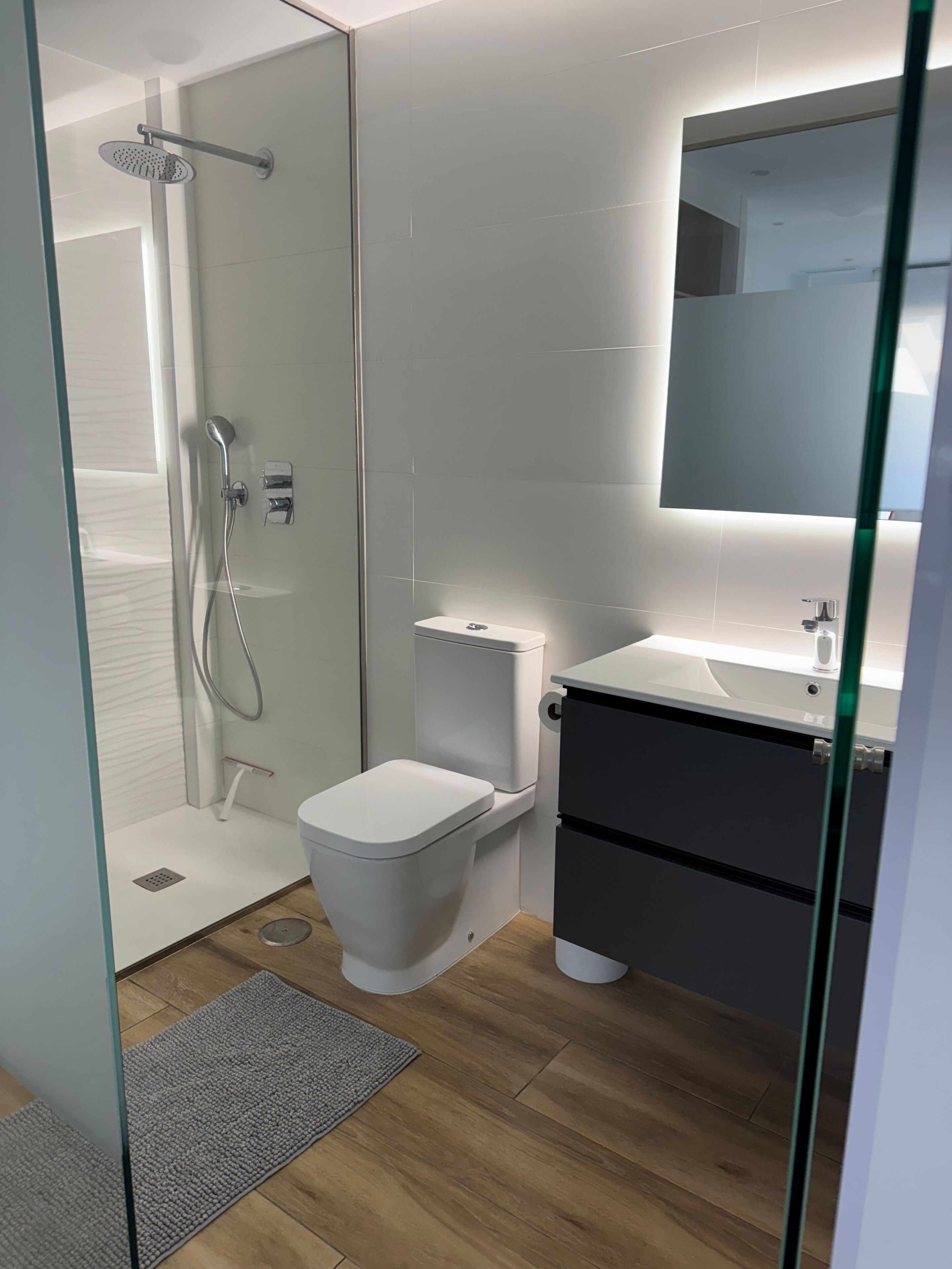 A modern bathroom with a glass shower enclosure, a white toilet, and a dark vanity with a mirror.