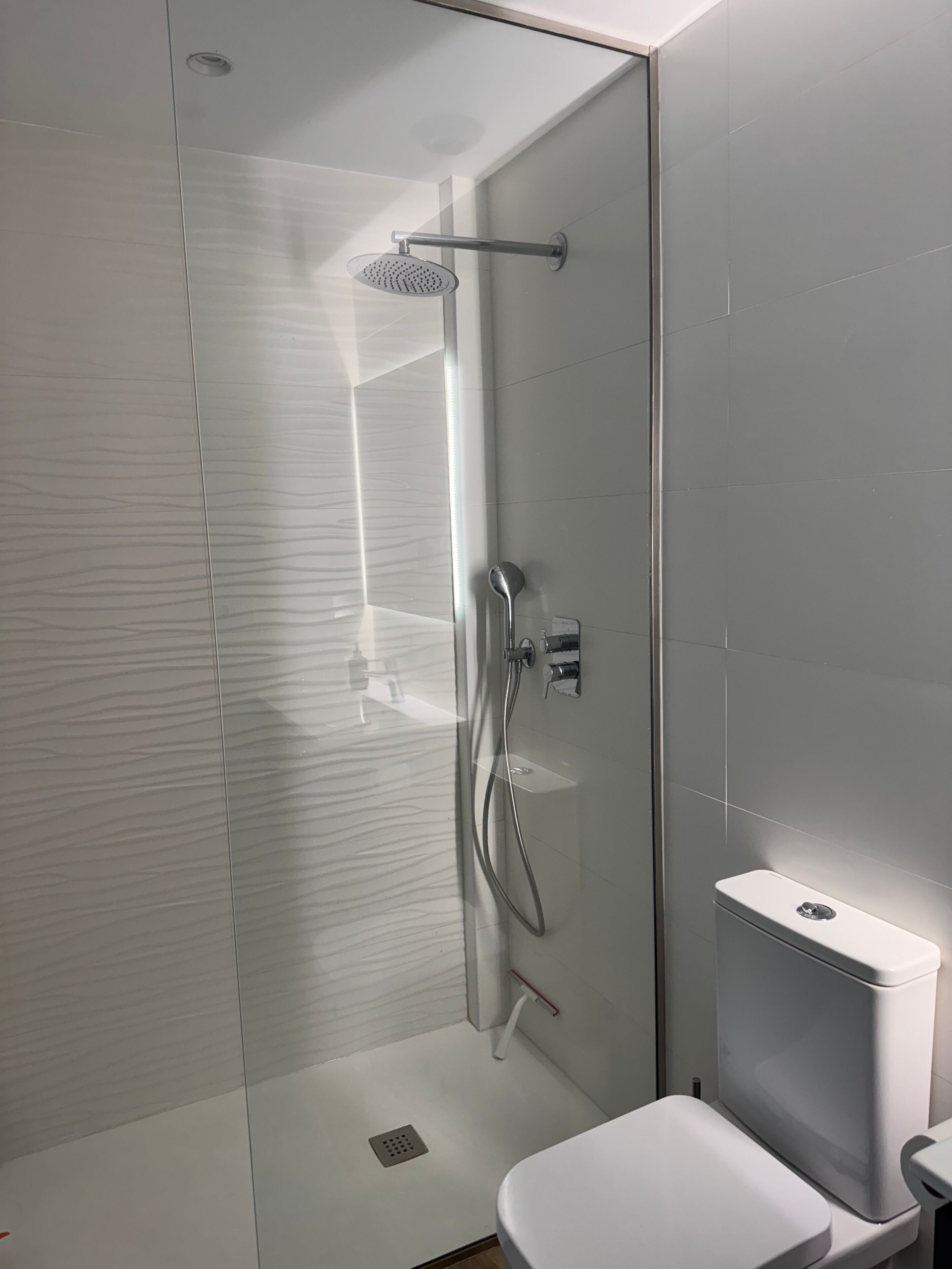 A modern bathroom with a glass-enclosed shower, a white toilet, and a sleek, minimalist design.