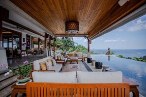An infinity pool with a view of the ocean, wooden furniture, and a covered seating area. - Villa ZeniMo, Surin Beach, pool, 9 BR 18 guests (Phuket)
