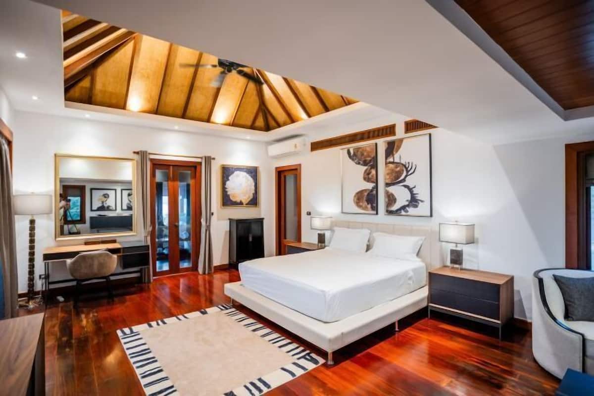A modern bedroom with a large bed, wooden flooring, a ceiling fan, and artwork on the walls.