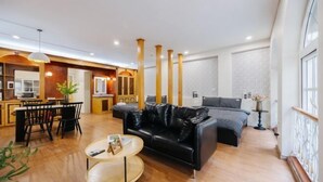 A modern living room with a black leather sofa, wooden flooring, and a dining area with a table and chairs. - VietHOME - 22 Pho Hue - Apartment 301 (Hanoi)