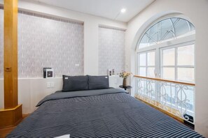 Un dormitorio con una cama grande, una mesita de noche, un ventanal y una barandilla de madera.