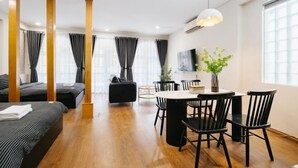 A modern hotel room with a wooden floor, a dining area with black chairs and a round table, and a large window with curtains. - VietHOME - 22 Pho Hue - Apartment 301 (Hanoi)