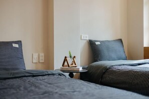 Una habitación de hotel con dos camas, una mesita de noche con una planta y un enchufe en la pared.