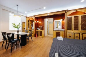 A hotel room with a wooden floor, a bed, a dining table with chairs, and a kitchen area. - VietHOME - 22 Pho Hue - Apartment 301 (Hanoi)