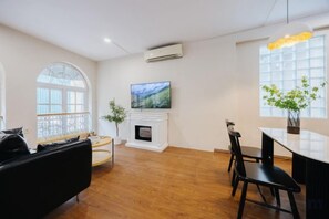 A modern living room with a fireplace, a television, and a dining area with chairs and a table. - VietHOME - 22 Pho Hue - Apartment 301 (Hanoi)