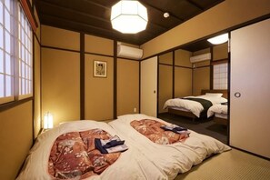 A traditional Japanese-style room with tatami flooring, two beds with bedding, a hanging light fixture, and a sliding door.