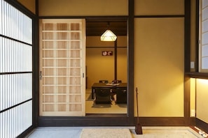 A traditional Japanese room with tatami flooring, a sliding door, a table with a hanging light, and a small shrine. - Miro Matsubara Takasegawa (Kyoto)