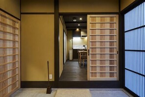Un interior japonés tradicional con puertas correderas, suelo de madera y una zona de comedor visible a través de la entrada.