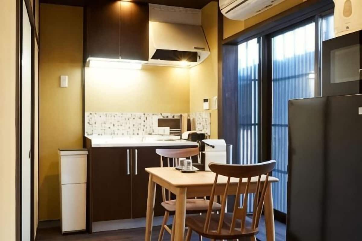 A compact kitchen with a dining area, a refrigerator, and a window with curtains.