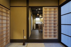 Un intérieur japonais traditionnel avec des portes coulissantes, un plancher en bois et un coin repas à l’arrière-plan.