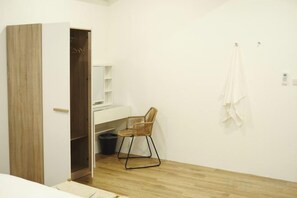 Une chambre avec une armoire en bois, un bureau blanc, une chaise et une serviette suspendue.