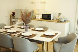 Un comedor con una mesa preparada para cuatro personas, un microondas y una pequeña cocina.