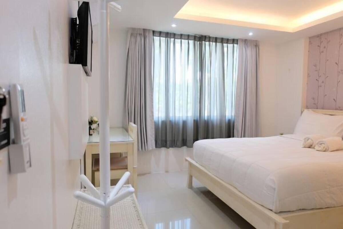 A modern hotel room with a large bed, a desk, and a TV mounted on the wall.