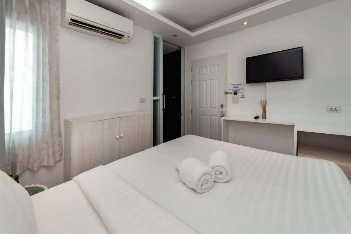A hotel room with a bed, a flat-screen TV mounted on the wall, and a window with curtains.