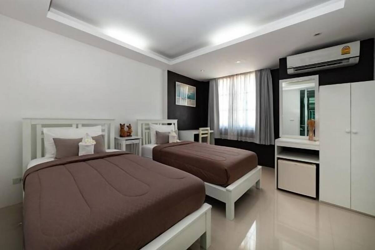 A modern hotel room with two beds, a desk, a wardrobe, and an air conditioning unit.
