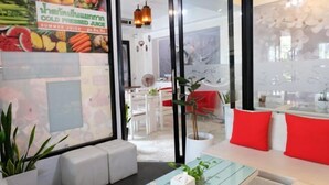 A modern interior with a seating area, a glass table, and a wall with a fruit and juice advertisement. - Baanpoon Apartment (Koh Samui)