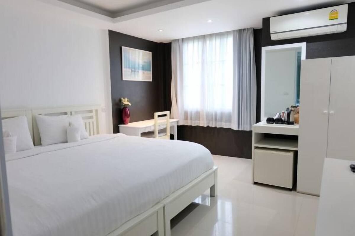 A hotel room with a bed, a desk, a chair, a wardrobe, and a window with curtains.