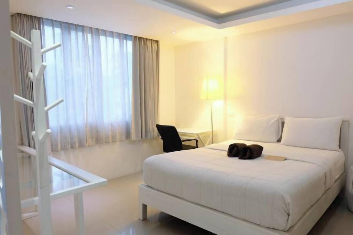 A hotel room with a bed, a desk, a chair, and a window with curtains.