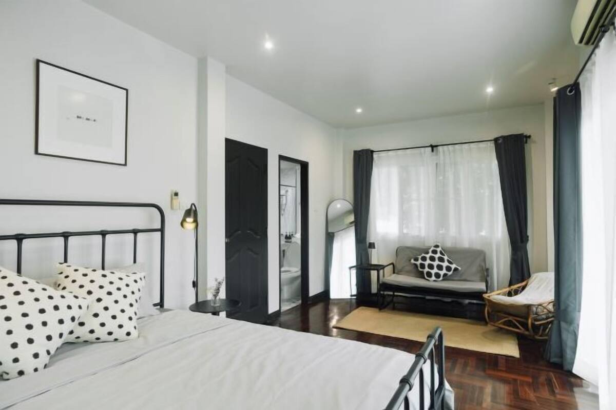 A modern bedroom with a bed, a chair, a sofa, and a window with curtains.