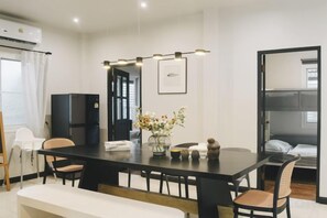 A modern hotel room with a dining table, chairs, a sofa, a bed, a black wardrobe, and a large window. - My Sukhumvit Villa (Bangkok)