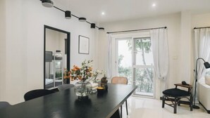 A modern dining area with a long table, chairs, a vase of flowers, and a view of the outdoors through a large window. - My Sukhumvit Villa (Bangkok)