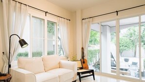 A spacious living room with a white sofa, a guitar, and large windows offering a view of the outdoors. - My Sukhumvit Villa (Bangkok)