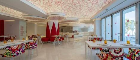 A modern dining area with tables and chairs, a patterned ceiling, and large windows.