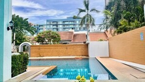 A swimming pool with a tiled deck, surrounded by a brick wall and palm trees.