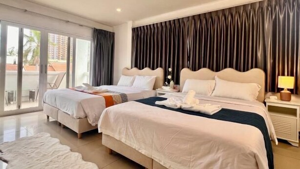 A hotel room with two beds, a ceiling fan, a large window with curtains, and a view of the outside.