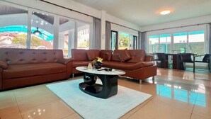 A spacious living room with a brown sectional sofa, a round coffee table, and a large window offering a view of the outside.