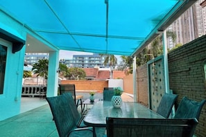 An outdoor patio area with a table and chairs, a blue canopy, and a view of buildings in the background. - Chasing Light Villa (Pattaya)