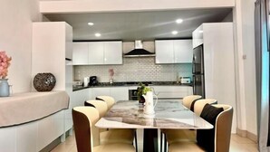 A modern kitchen with white cabinets, a marble countertop, and a dining area with a table and chairs.