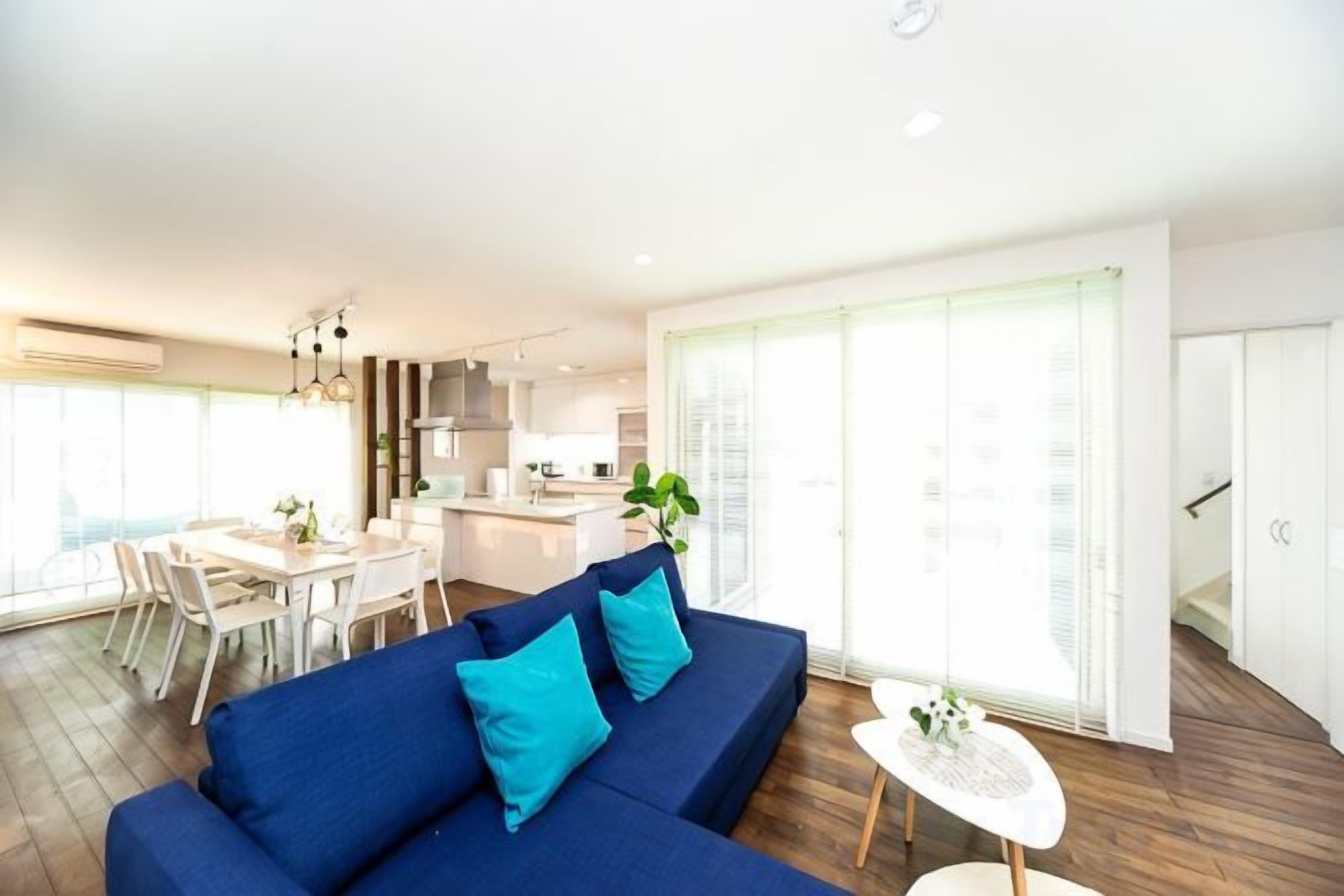 Un salon moderne avec un canapé bleu, un coin repas et une cuisine en arrière-plan.